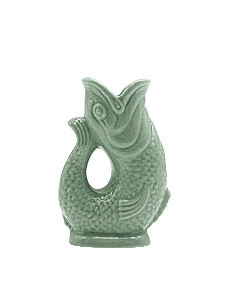 Die Gluckigluck Karaffe Mini Salbeigrün von Gluckigluck ist ein grünes, fischförmiges Keramikornament mit detaillierten Schuppen und offenem Maul, inspiriert vom klassischen Fisch-Karaffe-Design und aufrecht stehend auf einem kleinen Sockel.