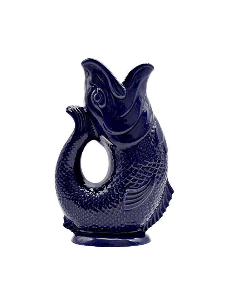 Die Gluckigluck Karaffe Large Kobalt Blau von Gluckigluck ist ein dunkelblauer Keramikkrug in Form eines Fisches mit offener Öffnung, strukturierten Schuppen und einem schwanzförmigen Griff – ein echtes englisches Original.