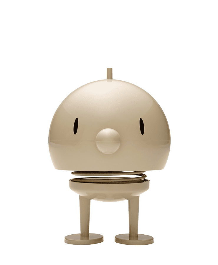 Die Hoptimist Bumble Large Latte Beige Figur von Hoptimist steht mit ovalen Augen, runder Nase, Federhals und flachen Beinen auf einer Fläche – ihr fröhliches Lächeln zaubert jedem ein Grinsen ins Gesicht.