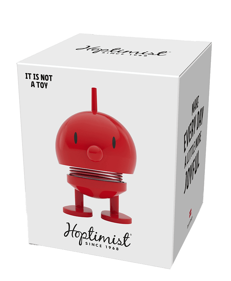 Eine weiße Schachtel zeigt den Hoptimist Bumble Small Red – eine ikonische rote, runde Figur mit Beinen und einem Federkreisel. Auf der Schachtel steht: KEIN SPIELZEUG, Hoptimist seit 1968 und MACHT JEDEN TAG EIN BISSCHEN FREUDE – perfekt für ein Lächeln!.