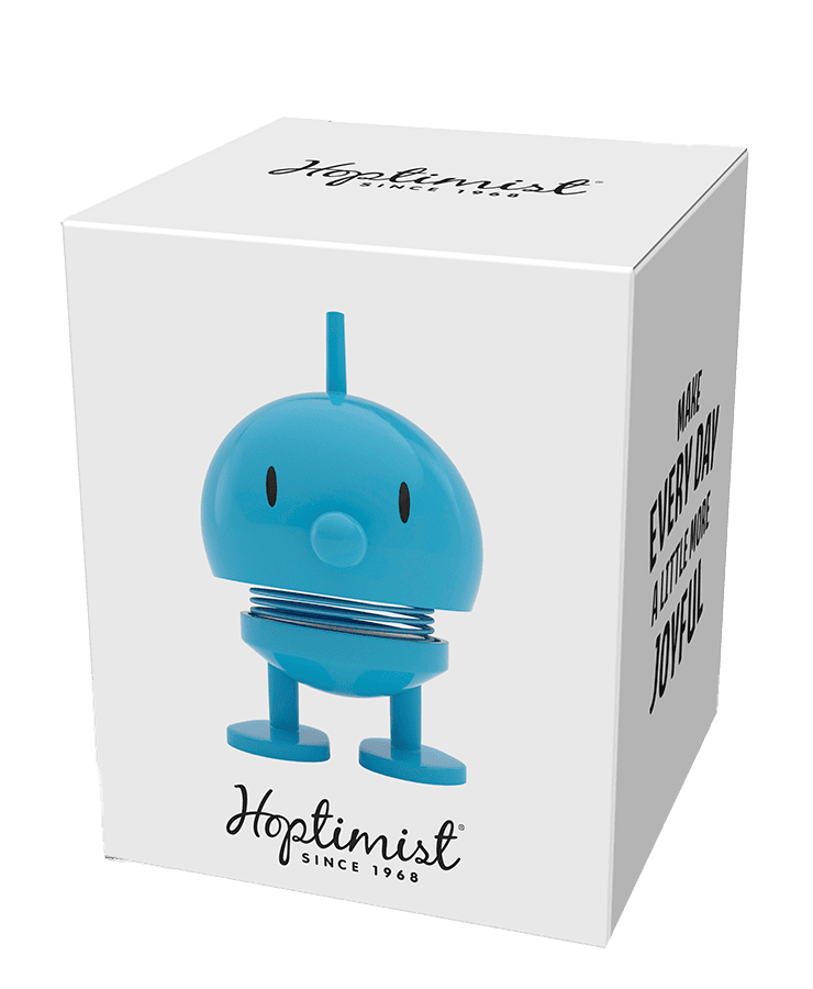 Eine weiße Schachtel zeigt die Hoptimist Bumble Small Türkis-Figur – ein rundes, federndes Design mit kleinen Beinen – von Hoptimist. Auf der Box steht „Make every day a little more joyful“ – inspiriert von Hoptimisten und einem optimistischen Lächeln.