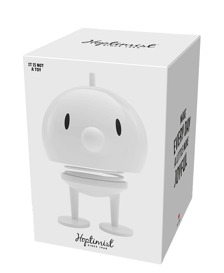 In einer weißen Schachtel befindet sich der Hoptimist Bumble Large White von Hoptimist – eine schlichte, runde Wackelkopffigur mit zwei Beinen. Auf der Schachtel steht „MACH JEDEN TAG EIN BISSCHEN FREUDEVOLLER“ und „ES IST KEIN SPIELZEUG“. Er weckt Optimismus und zaubert jeden Tag ein Lächeln ins Gesicht.