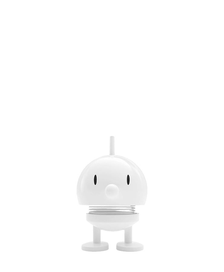 Der Hoptimist Bumble Small White von Hoptimist, eine kleine weiße runde Figur mit ovalen Augen, einer Punktnase, zwei Beinen und einem federnden Körper, steht aufrecht vor einem grünen Hintergrund und strahlt ein optimistisches Lächeln aus.