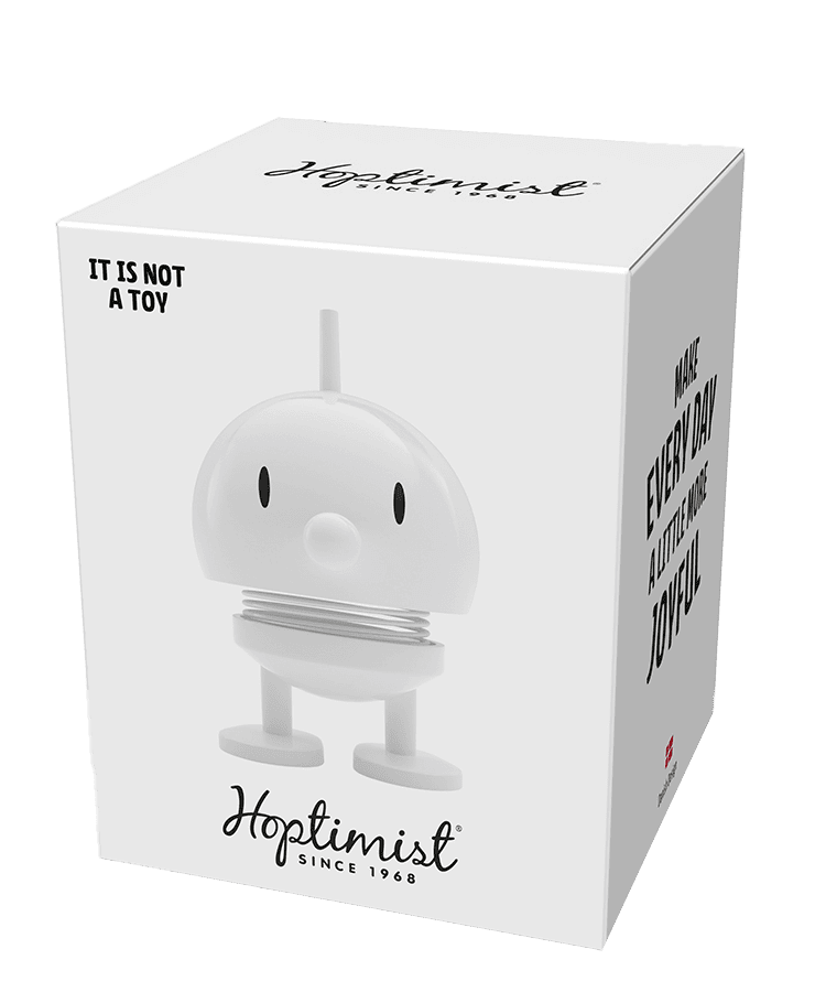 Eine weiße Schachtel zeigt den Hoptimisten Bumble Small White – eine niedliche, runde Figur mit federndem Körper und schlichtem Gesicht. Auf dem Karton stehen unter anderem „Hoptimist seit 1968“, „ES IST KEIN SPIELZEUG“ und „MACH JEDEN TAG AUTOMATISCH FREUDE“.