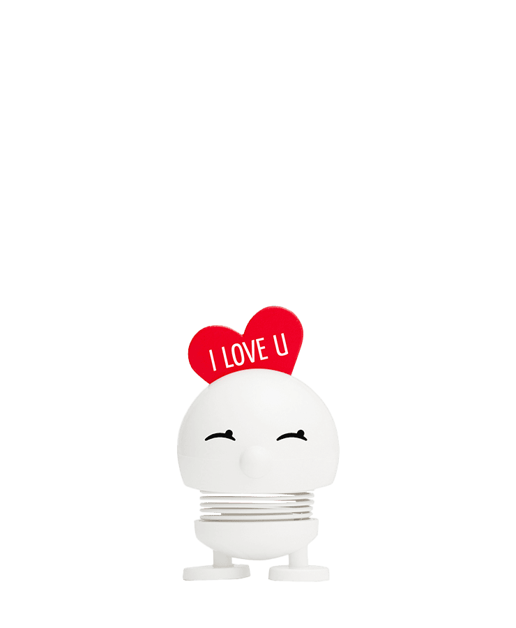 Der Hoptimist Love Bimble Small von Hoptimist ist eine weiße, federnde Figur mit einem lächelnden Gesicht, geschlossenen Augen und einem roten Herz mit der Aufschrift „I LOVE U“, inspiriert von den fröhlichen Designs von Gustav Ehrenreich.