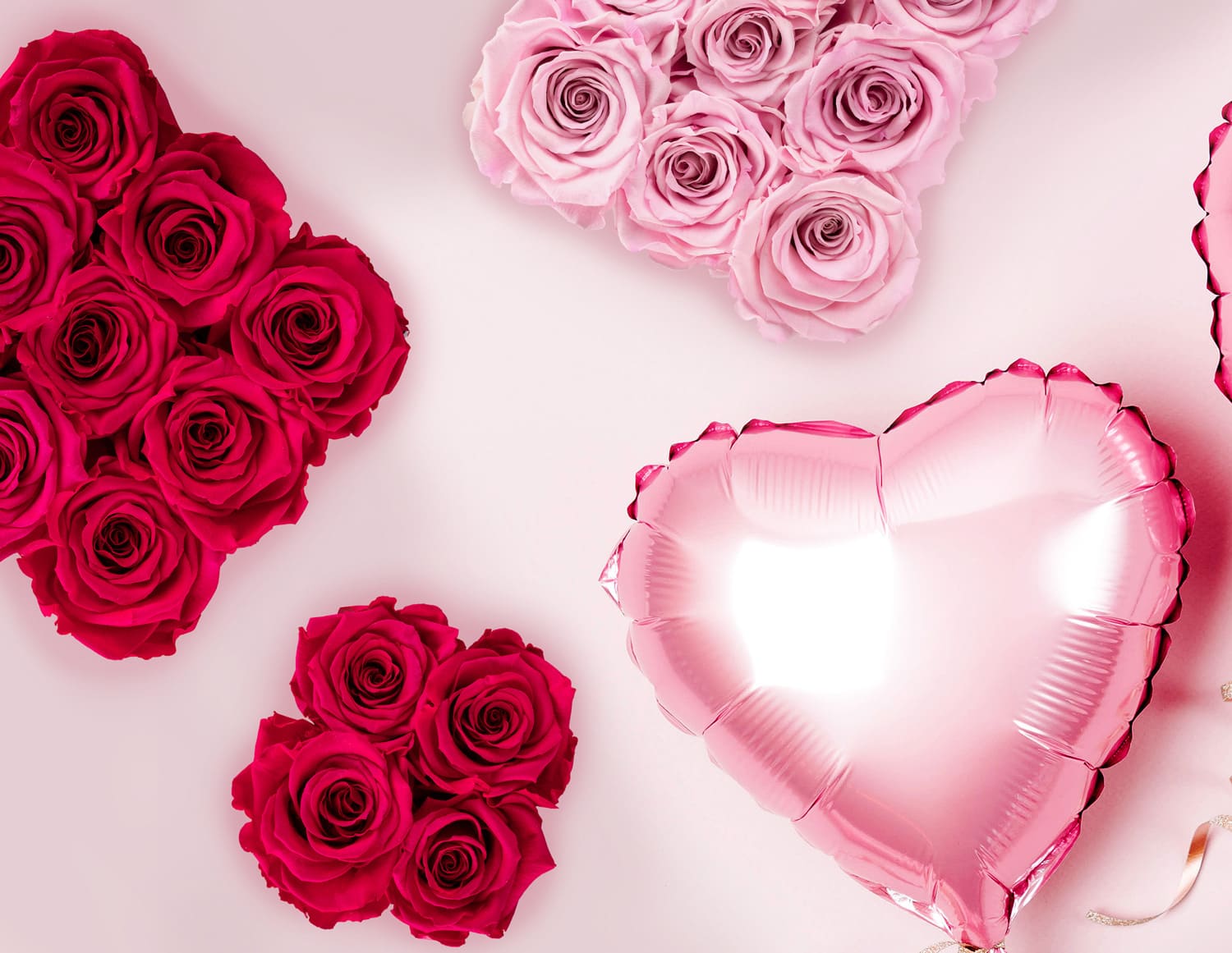 Herzförmige Arrangements aus roten und rosa Rosen umgeben einen glänzend rosa herzförmigen Ballon auf einem blassrosa Hintergrund.