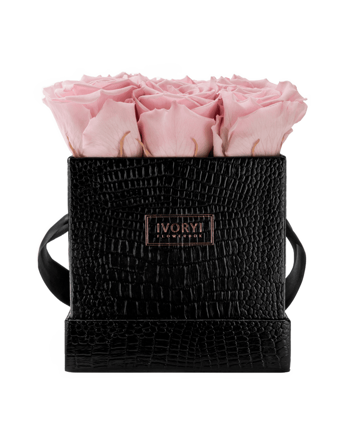 Die Ivoryi & Friends Flowerbox Medium Black Blush Rose besteht aus einer schwarzen strukturierten Box mit Griffen, einem roségoldenen „IVORY“-Etikett und einem Strauß hübsch arrangierter hellrosa konservierter Rosen.