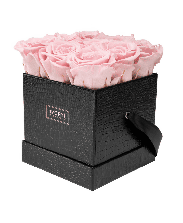 Die „Ivoryi Flowerbox Medium Black Blush Rose“ von Ivoryi & Friends ist eine schwarze, strukturierte Box mit einem Bandgriff und der Aufschrift IVORY, die innen mit hübsch angeordneten zartrosa Rosen gefüllt ist.