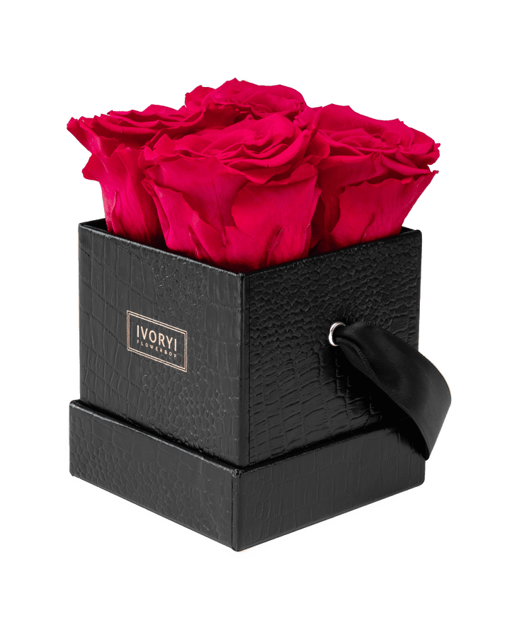 Eine kleine, schwarz strukturierte Ivoryi & Friends Blumenbox (New Pink) mit schwarzem Bandgriff enthält leuchtend rote, langlebige Rosen. Das goldene „IVORYI!“-Etikett fällt auf. Fotografiert vor weißem Hintergrund.