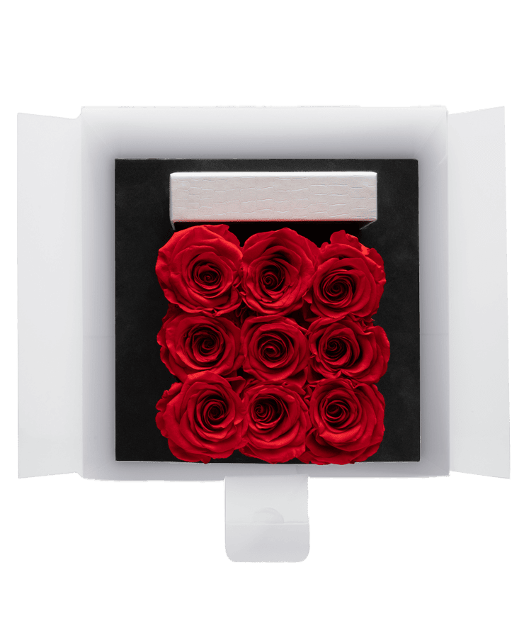 Eine Ivoryi & Friends Ivoryi Flowerbox Medium Perlmutt Romantic Red mit geöffnetem Deckel, mit neun konservierten Rosen in einem schwarzen Tablett und einer kleinen weißen Karte über den Blumen.