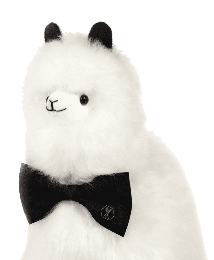 Das Alpaka Stofftier PACO Pearl White von Weich Couture Alpaka ist ein flauschiges weißes Alpaka-Plüschtier mit schwarzen Ohren und einer königlichen PACO das Alpaka Fliege mit einem kleinen Emblem, abgebildet auf transparentem Hintergrund.