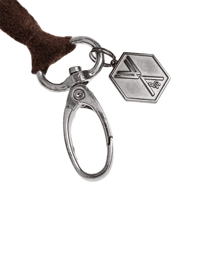 Der Alpaka Pompon CLAVE Anhänger Taupe von Weich Couture Alpaka verfügt über einen taupefarbenen Anhänger mit geprägtem Design, der an einem Federverschluss befestigt ist – ideal, um Ihrer Handtasche Eleganz zu verleihen.