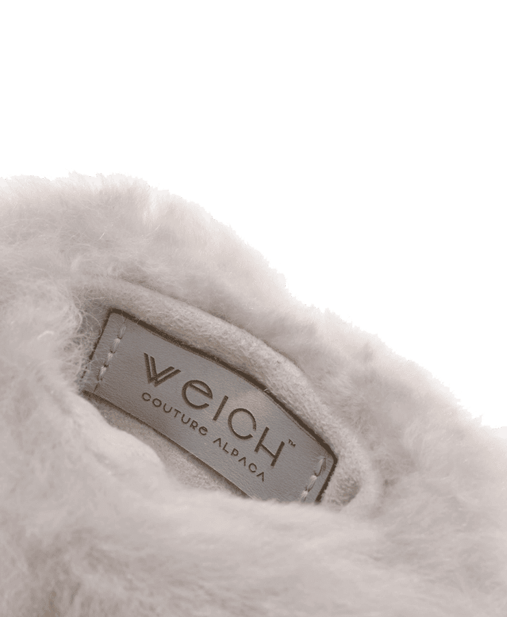 Nahaufnahme des weichen, flauschigen silbergrauen Stoffes der Weich Couture Alpaka Wärmflasche Regular mit eingenähtem Etikett. Die luxuriöse Textur vermittelt Komfort und ist ideal für alle, die kuschelige Wärme suchen.